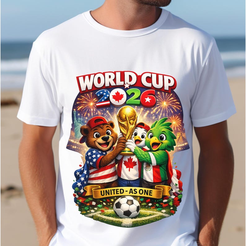 May include: White t-shirt featuring a colorful graphic for the 2026 World Cup. The design includes cartoon mascots holding the World Cup trophy, fireworks, and the text "WORLD CUP 2026" and "UNITED - AS ONE". A soccer ball is at the bottom.