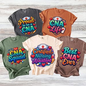 Pode incluir: Cinco camisetas coloridas com vários designs relacionados a Assistentes de Enfermagem Certificados (CNA). Cada camisa apresenta textos como "Proud to be a CNA", "CNA Life" e "Best CNA Ever", juntamente com gráficos de tema médico em cores vibrantes. As camisas são exibidas em um fundo de madeira clara.