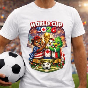 May include: White t-shirt featuring a colorful graphic for the 2026 World Cup. The design includes cartoon mascots holding the World Cup trophy, fireworks, and the text "WORLD CUP 2026" and "UNITED AS ONE". A soccer ball is also featured.
