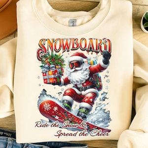 May include: Cream-colored sweatshirt featuring a graphic of Santa Claus snowboarding. Santa is wearing a red suit, goggles, and a white beard, holding a gift and riding a red snowboard. The text "SNOWBOARD" and "Ride the Snow & Spread the Cheer" are displayed.