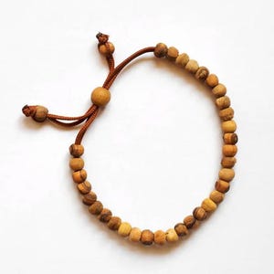 May include: A brown wooden bead bracelet with a brown cord and adjustable closure. The bracelet is made of natural wood beads.