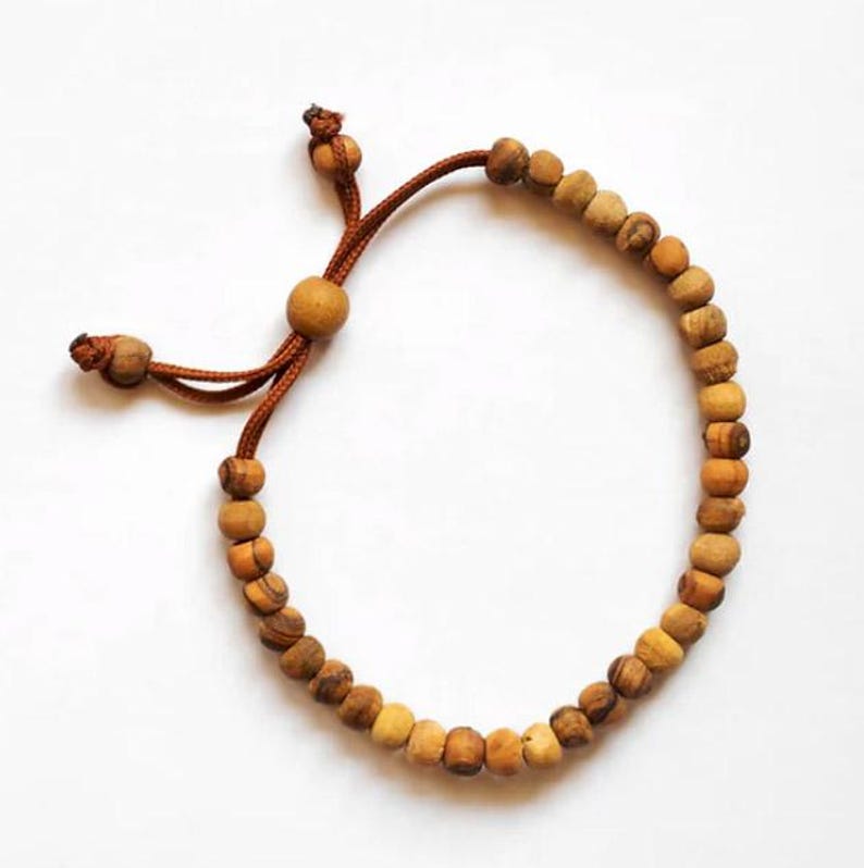 May include: A brown wooden bead bracelet with a brown cord and adjustable closure. The bracelet is made of natural wood beads.