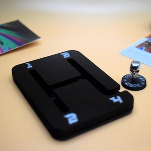 May include: A black plastic dice tray with a 'H' shaped cutout and white numbers 1, 2, 3, and 4 on the sides. A silver skull miniature is on a black base.