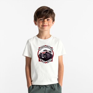 以下が含まれることがあります： 白いTシャツに、赤と黒のモンスタートラックのグラフィックがプリントされています。テキストは「Taylor's 4th Jam」です。