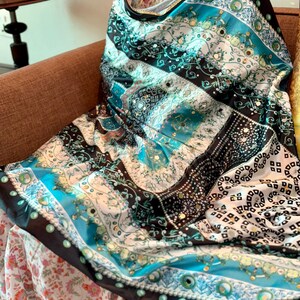 Peut inclure: Un châle à motifs avec un mélange de motifs turquoise, noirs et blancs. Le châle présente des motifs complexes, notamment des formes florales et géométriques, avec une bordure turquoise et noire. Le tissu semble soyeux.