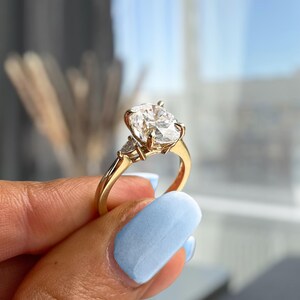Op de afbeelding: Een gouden verlovingsring met een grote ovale diamant en twee kleinere driehoekige diamanten aan weerszijden.