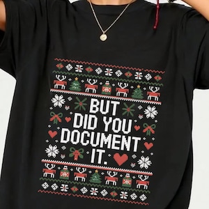May include: Black t-shirt featuring a festive, pixelated design with reindeer, Christmas trees, snowflakes, and the text "BUT DID YOU DOCUMENT IT." The shirt has a crew neck and short sleeves.