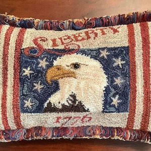 May include: A red, white, and blue throw pillow with a fringed border. The pillow features an embroidered bald eagle with the words "Liberty 1776".