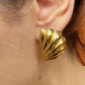 Puede incluir: Pendientes de clip dorados y texturizados. Los pendientes tienen un diseño esculpido en forma de abanico con líneas curvas. Los pendientes son de color oro cálido y brillante. Los pendientes son de estilo vintage.