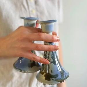 May include: Two ceramic candle holders in a blue and brown glaze. The holders have a flared base and a wide opening at the top.