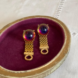 May include: Two vintage earrings featuring iridescent, orb-shaped stones. The stones are set on gold-coloured metal with a chain-link design and a small, circular clasp. The earrings are presented in a velvet-lined, oval jewellery box.
