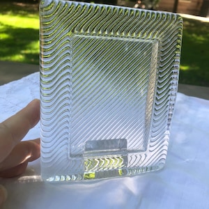 May include: A rectangular glass picture frame featuring a clear center panel with diagonal etched lines. The border of the frame is composed of a thick, textured glass with a repeating wavy pattern that creates a distinct visual contrast.