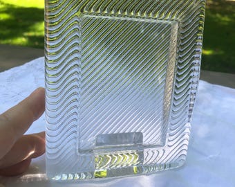May include: A rectangular glass picture frame featuring a clear center panel with diagonal etched lines. The border of the frame is composed of a thick, textured glass with a repeating wavy pattern that creates a distinct visual contrast.
