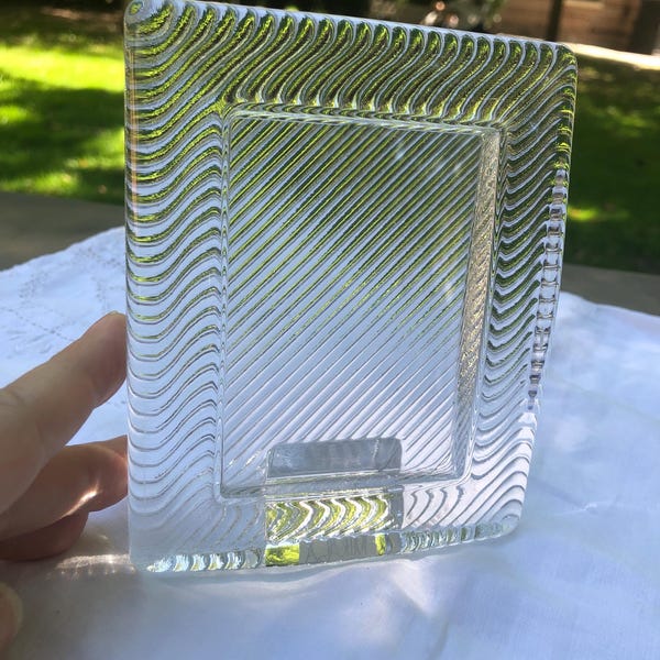 May include: A rectangular glass picture frame featuring a clear center panel with diagonal etched lines. The border of the frame is composed of a thick, textured glass with a repeating wavy pattern that creates a distinct visual contrast.