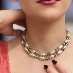 May include: A double-strand necklace featuring oval-shaped, metallic silver-toned beads with a textured, hammered finish. The beads are separated by small, intricate, dark-toned metal spacers, creating a layered look around the neck.