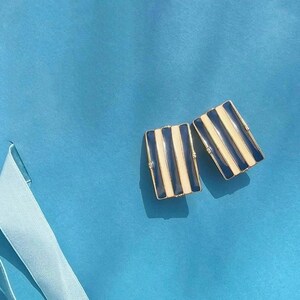 Könnte beinhalten: Ein Paar goldfarbene Ohrringe mit einem schwarz-weiß gestreiften Design. Die Ohrringe sind rechteckig.