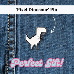 Pode incluir: Um alfinete de dinossauro pixelizado branco com contornos pretos é exibido em um fundo de ganga azul. O texto "'Pixel Dinosaur' Pin" está no topo e "Perfect Gift!" na parte inferior. O alfinete é um acessório de estilo retro.