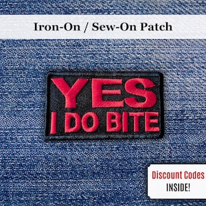 Może przedstawiać: Czarna, prostokątna naszywka z czerwonym napisem "YES I DO BITE". Naszywka znajduje się na niebieskim tle z dżinsu. Obraz zawiera również mały biały prostokąt z napisem "Discount Codes INSIDE!"