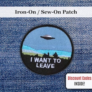 May include: Circular embroidered patch with a black border. The patch depicts a blue sky with a UFO, a landscape, and the text "I WANT TO LEAVE". It is an iron-on or sew-on patch.