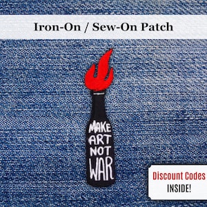 Może przedstawiać: Naszywka do naprasowywania przedstawiająca czarną butelkę z czerwonym płomieniem i białym napisem "MAKE ART NOT WAR". Naszywka znajduje się na niebieskim tle z dżinsu. U góry znajduje się napis "Iron-On / Sew-On Patch".