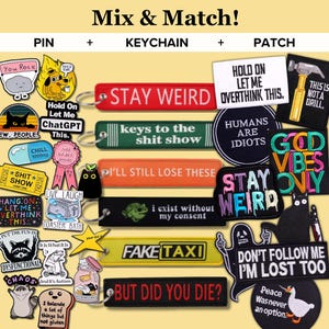 Puede incluir: Una colección de pines, llaveros y parches con frases y gráficos humorísticos. Los artículos incluyen frases como "Stay Weird", "Fake Taxi" y "But Did You Die?" con varios diseños y colores.