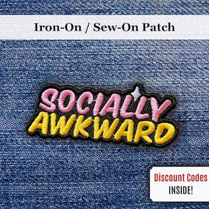 Può includere: Toppa termoadesiva o da cucire con la scritta "SOCIALLY AWKWARD" in ricamo rosa e giallo su sfondo nero. La toppa è su uno sfondo di denim blu. Un piccolo rettangolo bianco con la scritta "Discount Codes INSIDE!" si trova nell'angolo in basso a destra.