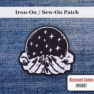 May include: Black and white iron-on patch featuring a crystal ball design with stars, held by two hands. The patch has the text "Iron-On / Sew-On Patch" and "Discount Codes INSIDE!"