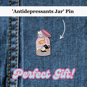 May include: A pink enamel pin featuring a glass jar filled with cartoon cats. The jar is labelled "Anti Depressants". The pin is displayed on a blue denim background with the text "Perfect Gift!" in a retro font.