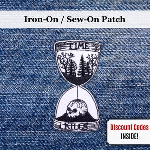 May include: An iron-on patch with an hourglass design, the words "TIME" and "KILLS" are visible. The top section shows a forest, the bottom a skull. The patch is set against a blue denim background.