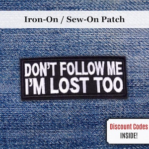 Puede incluir: Un parche rectangular en blanco y negro con el texto "DON'T FOLLOW ME I'M LOST TOO". El parche está sobre un fondo de mezclilla azul. Las palabras "Iron-On / Sew-On Patch" están encima del parche.