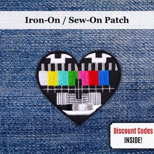 Pode incluir: Patch em forma de coração para passar a ferro com um design de padrão de teste colorido. O patch apresenta uma borda preta e uma exibição vibrante de cores, incluindo amarelo, ciano, verde, magenta e vermelho. O texto "Iron-On / Sew-On Patch" está no topo.