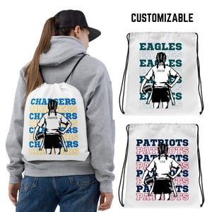 May include: White drawstring bag with a black and white illustration of a girl holding a football. The bag has the text "CHARGERS" repeated in blue and yellow with the name "HARPER" in black. A second white drawstring bag with a black and white illustration of a girl holding a football. The bag has the text "PATRIOTS" repeated in red and blue with the name "LILA" in black. A third white drawstring bag with a black and white illustration of a girl holding a football. The bag has the text "EAGLES" repeated in green and white with the name "CHLOE" in black.