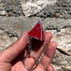 Puede incluir: Un llavero de metal rojo con forma de triángulo con una cadena y un anillo plateados.