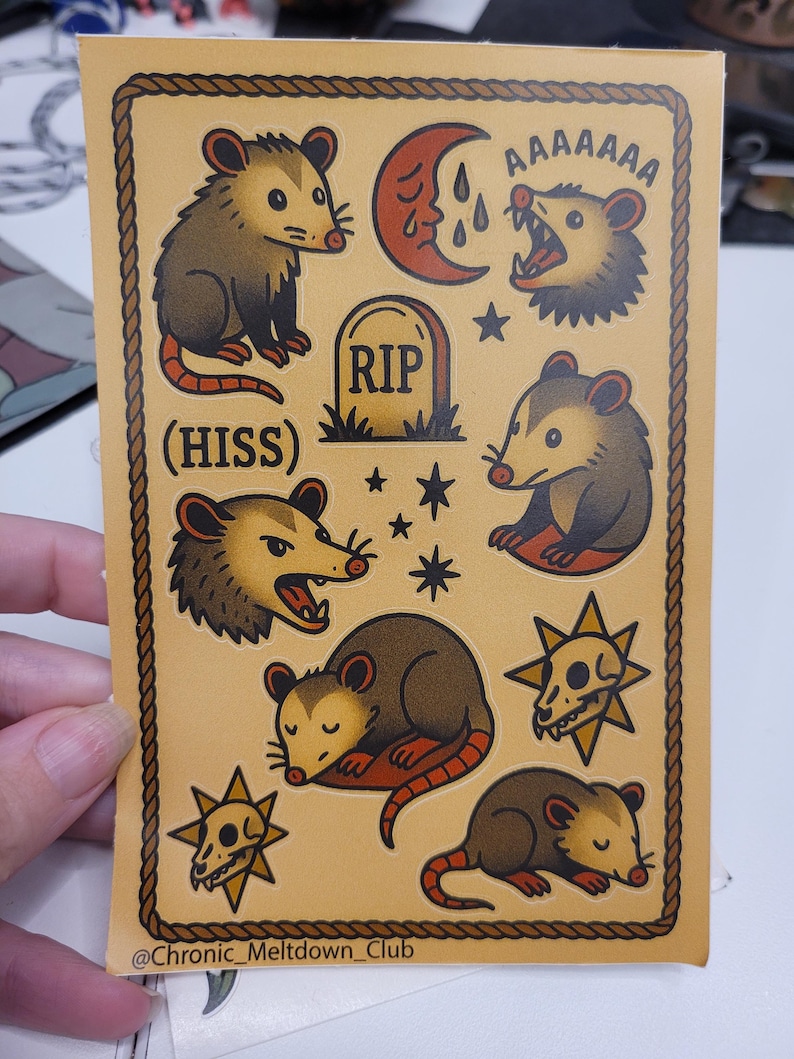 May include: A sticker sheet with a tan background and a brown rope border. The sheet features various opossum illustrations, a tombstone, a crying moon, stars, and a skull. Text includes "(HISS)" and "AAAAAAA". The artist's name is also included.