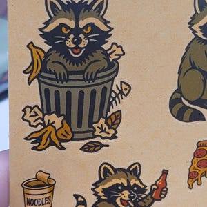 May include: A sheet of raccoon-themed stickers. One raccoon is in a trash can with a banana peel and fish bones. Another raccoon holds a bottle and a taco. A cup of noodles and a slice of pizza are also shown.