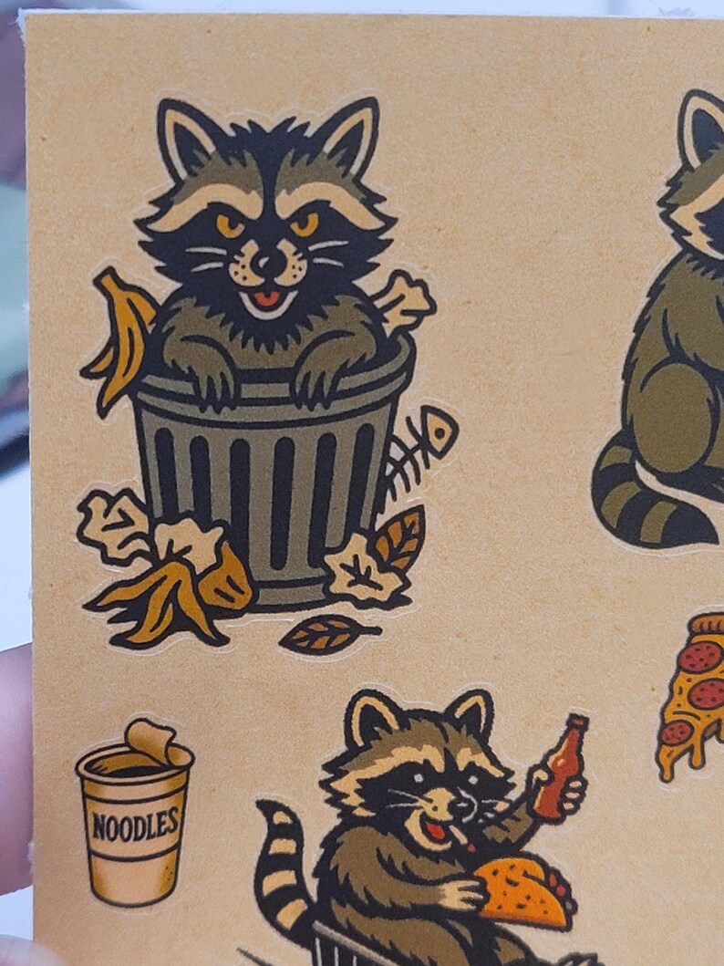 May include: A sheet of raccoon-themed stickers. One raccoon is in a trash can with a banana peel and fish bones. Another raccoon holds a bottle and a taco. A cup of noodles and a slice of pizza are also shown.