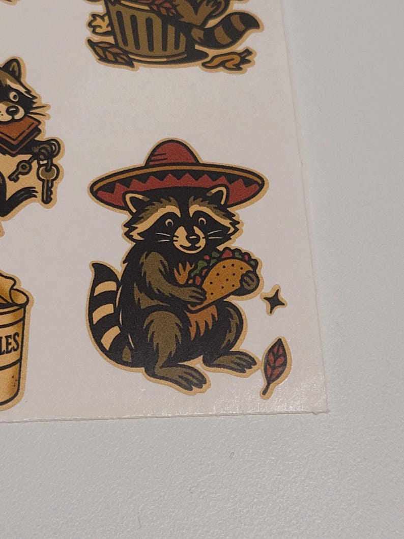 May include: A sheet of stickers featuring cartoon raccoons. One raccoon wears a sombrero and holds a taco. Other raccoons are depicted with keys, in a trash can, and with a tail. The stickers have a vintage, hand-drawn style.