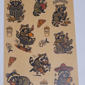 May include: A sheet of raccoon-themed stickers on a tan background. The stickers feature raccoons in various poses, including eating pizza, holding beer, and wearing a sombrero. Other images include pizza slices, noodles, and fish bones.