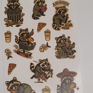 May include: Sheet of stickers featuring cartoon raccoons in various poses. One raccoon is in a trash can, another holds a heart, and others eat pizza and drink beer. The word "NOODLES" is on a cup.