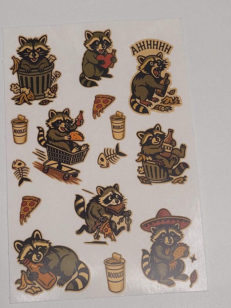 May include: Sheet of stickers featuring cartoon raccoons in various poses. One raccoon is in a trash can, another holds a heart, and others eat pizza and drink beer. The word "NOODLES" is on a cup.