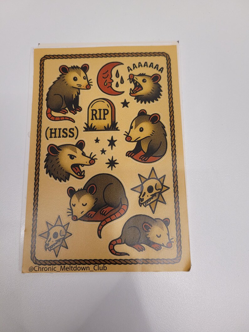 May include: A sticker sheet featuring opossum illustrations in a vintage tattoo style. The opossums are depicted in various poses, with text that reads "AAAAAAA" and "(HISS)". The design includes a RIP tombstone, stars, and a crescent moon.