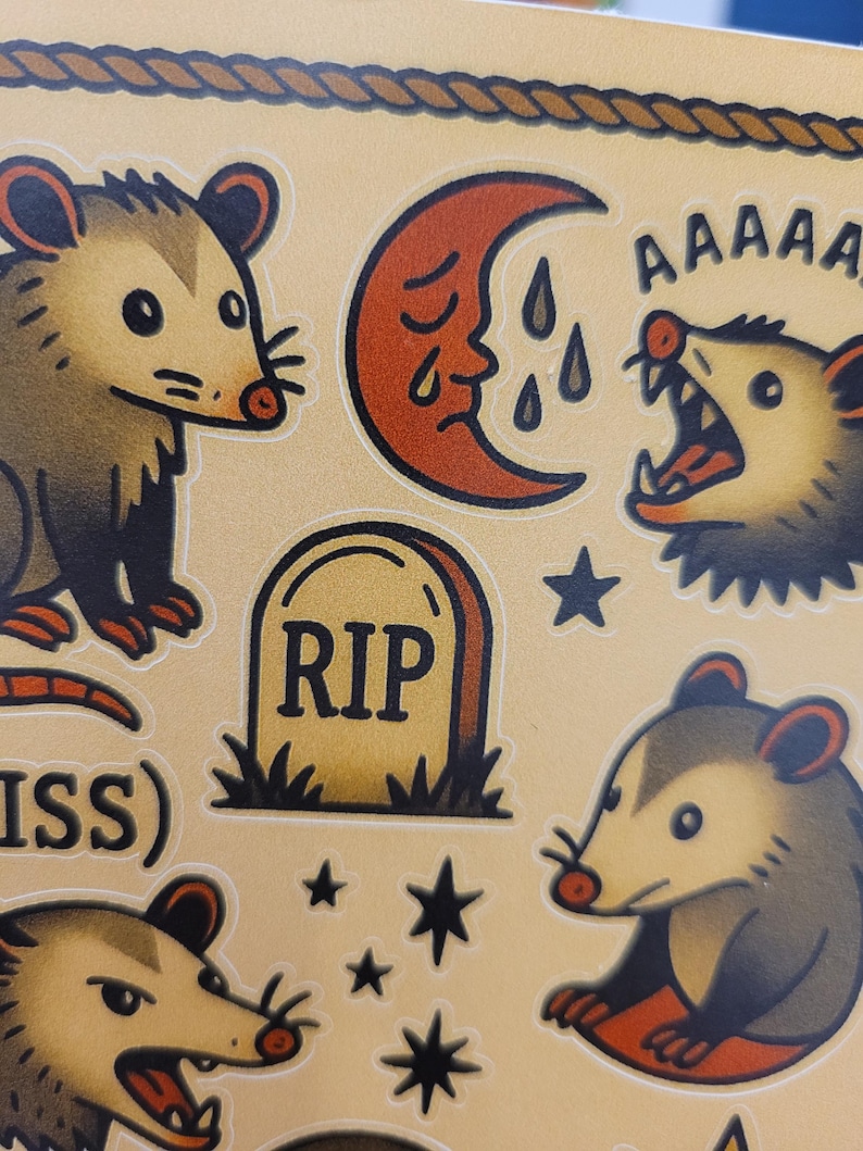 May include: A sheet of stickers featuring opossum illustrations in a traditional tattoo style. Designs include opossums, a crying moon, a tombstone with "RIP", and stars. The color palette is primarily tan, brown, and red.