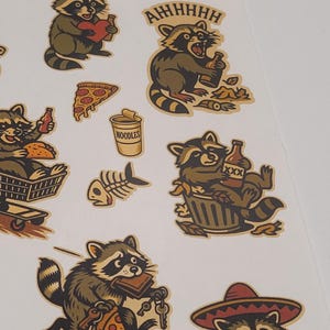 May include: Sheet of raccoon stickers in various poses, holding a heart, a bottle, pizza, and keys. One sticker has the text "AHHHHH". The stickers are in shades of brown, tan, and black, with a white background.