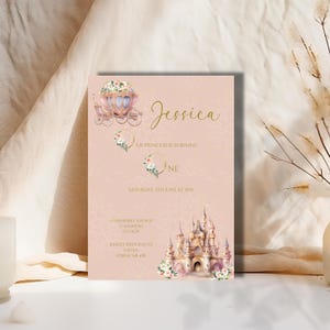Könnte beinhalten: Eine rosafarbene und goldene Prinzessinnen-Einladung zum ersten Geburtstag mit einer Kutsche, einem Schloss und Blumen. Die Einladung lautet "Unsere Prinzessin wird eins" und enthält das Datum und die Uhrzeit der Party. Sie enthält auch die Adresse und die Kontaktinformationen für die RSVP.