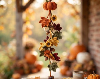 May include: A hanging crochet decoration featuring a central orange pumpkin at the top, followed by a vertical arrangement of crocheted autumn leaves in shades of red, orange, yellow, and green, small sunflowers, and brown acorns on a string.