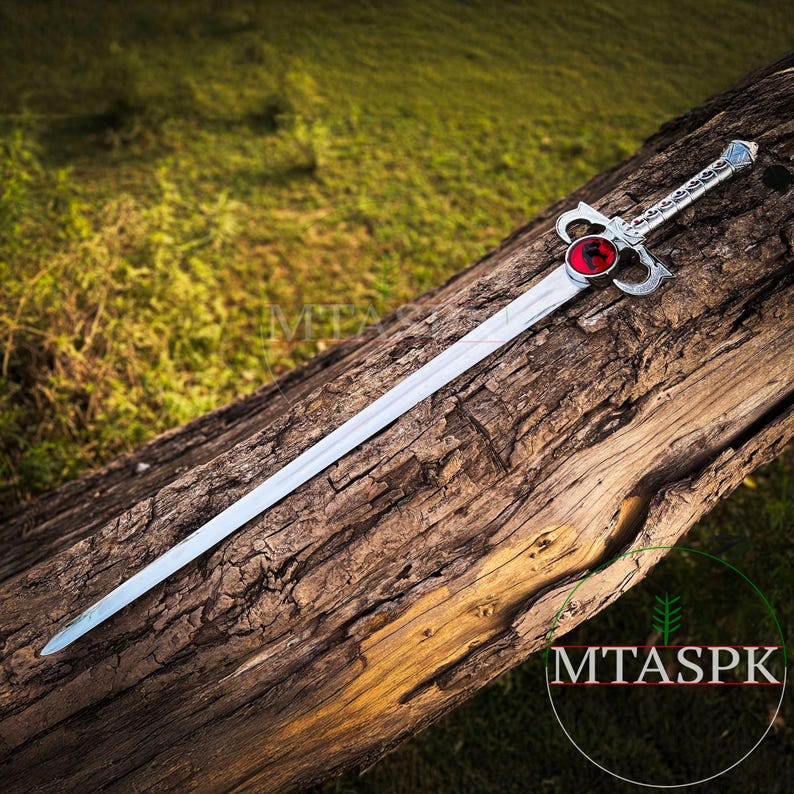 May include: A silver sword with a red jewel in the pommel. The sword is lying on a wooden log.