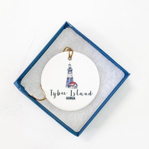 Puede incluir: Adorno de cer&aacute;mica blanca con una ilustraci&oacute;n de acuarela del faro de Tybee Island en Georgia. El adorno tiene una cuerda dorada para colgar.