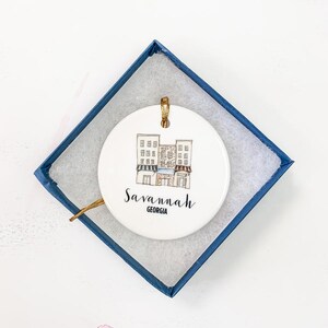 Puede incluir: Un adorno de cer&aacute;mica blanca con una ilustraci&oacute;n dibujada a mano de un edificio con el texto "Savannah, Georgia" en la parte delantera.