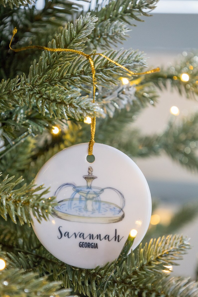 Puede incluir: Adorno navide&ntilde;o redondo blanco con una ilustraci&oacute;n azul y verde de una fuente y el texto "Savannah, Georgia".