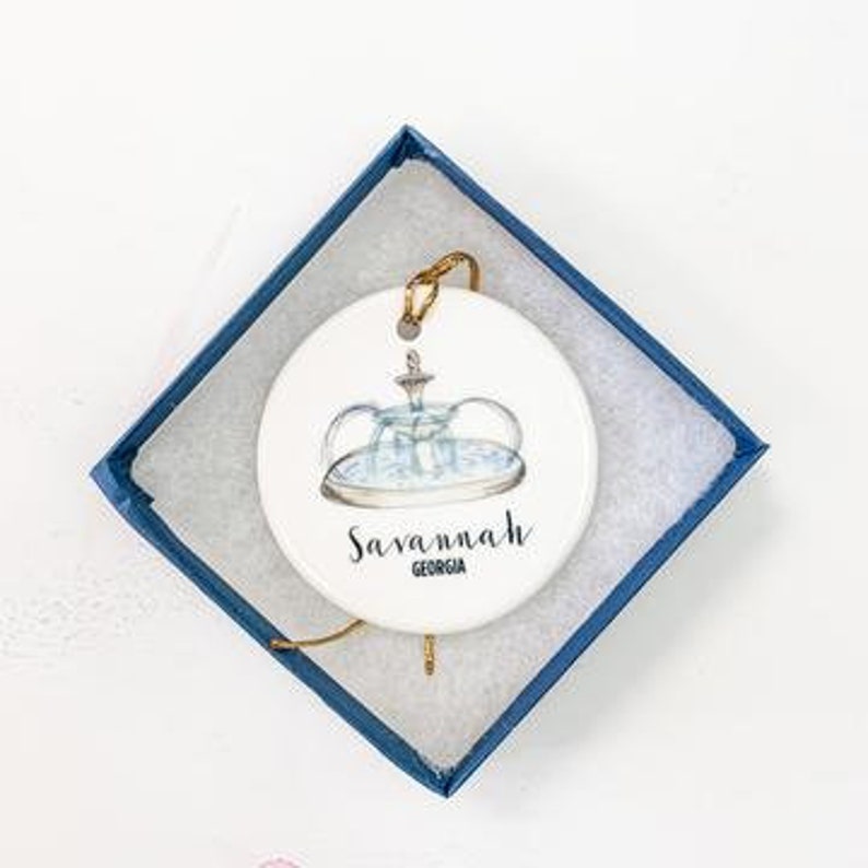 Puede incluir: Adorno de cer&aacute;mica blanca con una ilustraci&oacute;n azul y blanca de una fuente y el texto "Savannah, Georgia".